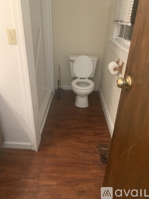 A white toilet in a small bathroom with wood flooring and a white door.