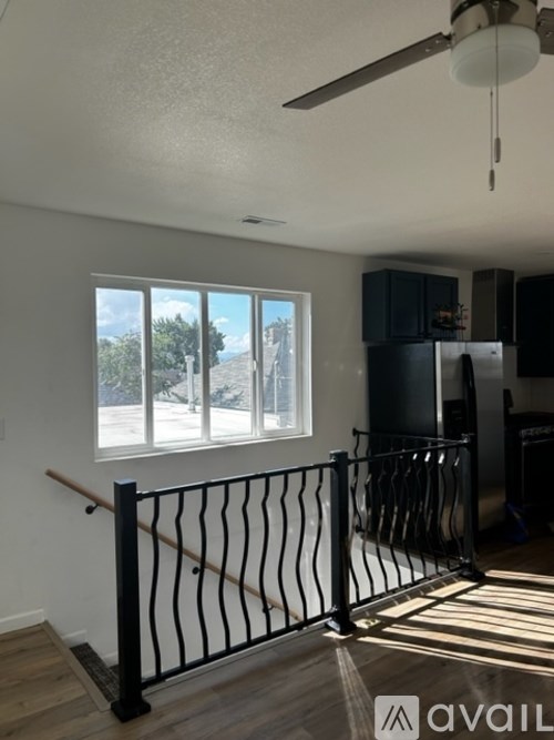 A room with a ceiling fan and a window with a view of trees and a building outside.
