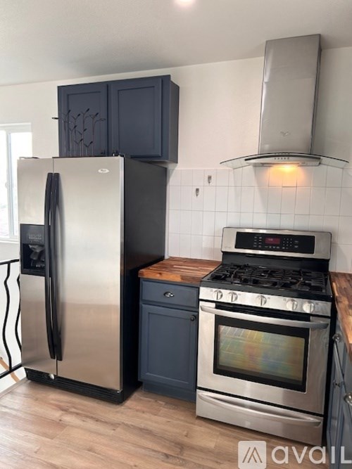 A kitchen with a stainless steel refrigerator and oven, black cabinets, and a wooden countertop.