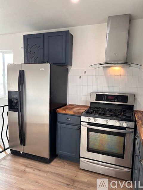 A kitchen with a stainless steel refrigerator and oven, black cabinets, and a wooden countertop.