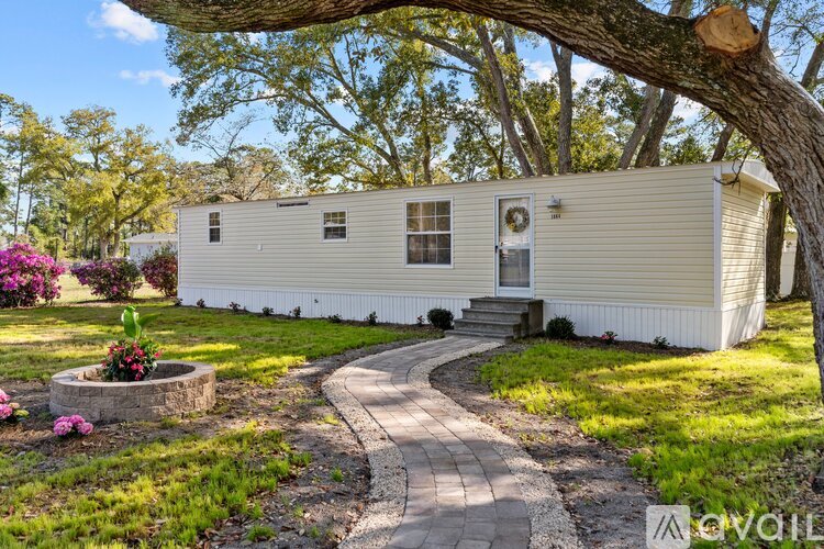 A mobile home is surrounded by a well-kept lawn and a variety of trees.