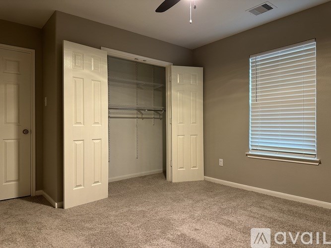 A room with a carpeted floor, a ceiling fan, and a window with blinds.