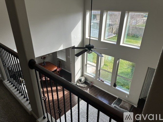 A room with a ceiling fan and a view of a yard through the windows.