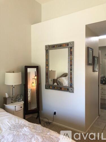 A bedroom with a bed, nightstand, lamp, and a large mirror on the wall.
