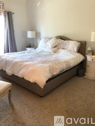 A bed with a white comforter and pillows sits in a room with a carpeted floor.
