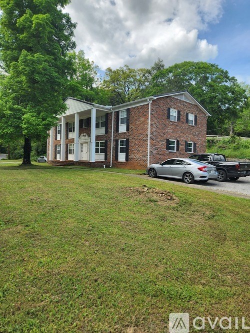 A brick building with a white door and windows is surrounded by greenery.