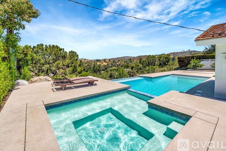 A swimming pool surrounded by a concrete patio and a white house.