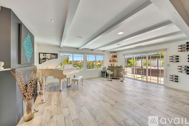A spacious living room with a grand piano and a view of the outdoors through large windows.