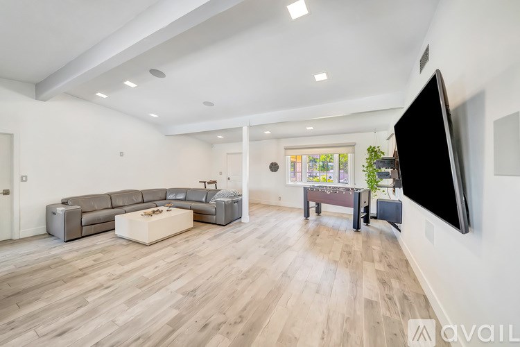A spacious living room with a grey sectional sofa, a white coffee table, and a flat-screen TV mounted on the wall.
