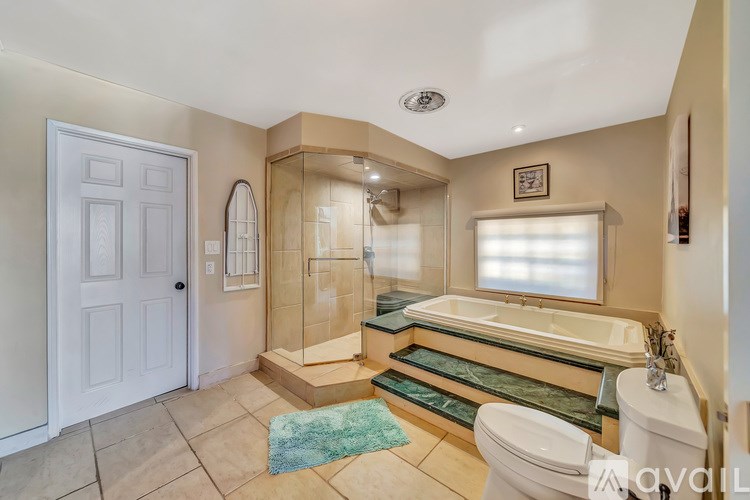 A bathroom with a white door, a bathtub, a toilet, and a window.