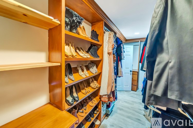 A walk-in closet with wooden shelves and a variety of shoes and clothes.