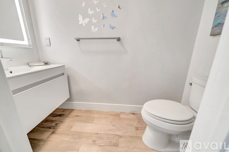 A white toilet sits in a bathroom with wooden flooring and white walls.