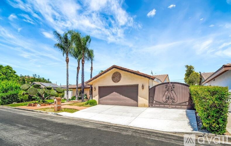A house with a brown garage door is surrounded by greenery and other houses.