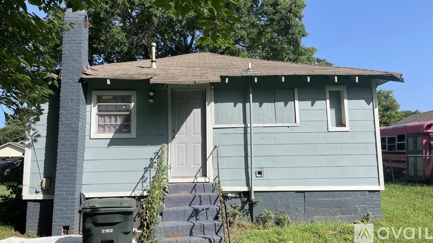 A blue house with a white door and a green trash can in front.