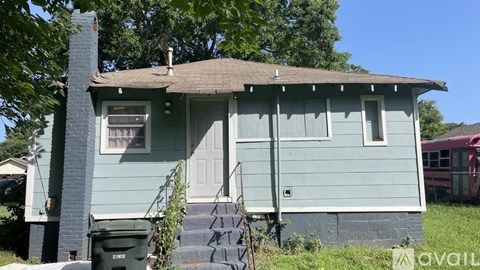 A blue house with a white door and a green trash can in front.