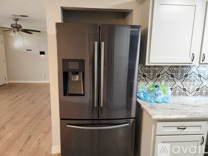 A modern kitchen with a stainless steel refrigerator and wooden flooring.