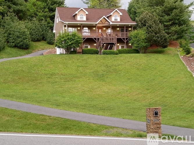 A large house with a brown roof and a balcony is surrounded by green grass and trees.