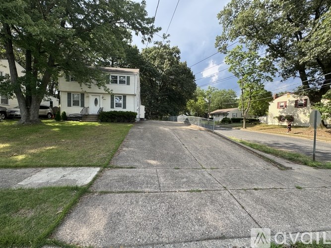 A residential street with a white house on the left and a tree-lined sidewalk.