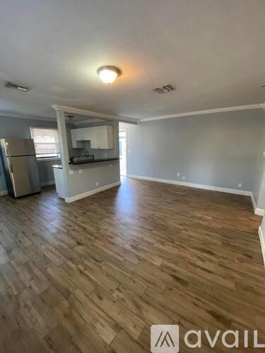A room with wooden flooring and a kitchen area in the background.