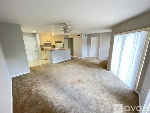 A carpeted room with a kitchen in the background.