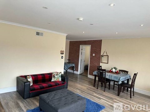 A living room with a red and black plaid couch, a black ottoman, and a dining table set for four.