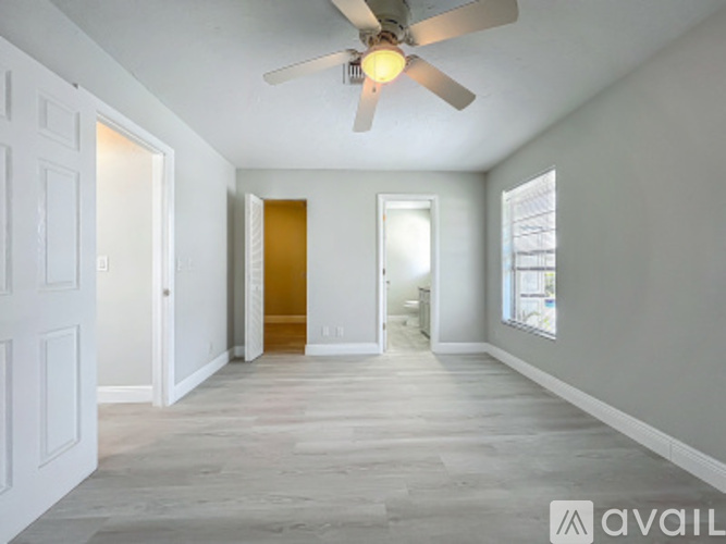 A spacious room with a ceiling fan and light, hardwood floors, and white walls.
