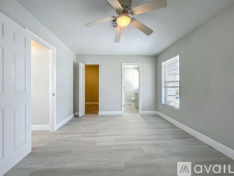 A spacious room with a ceiling fan and light, hardwood floors, and white walls.