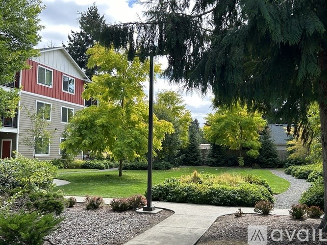 A house with a red roof and a white exterior is surrounded by a garden with a gravel path leading to a black lamp post.