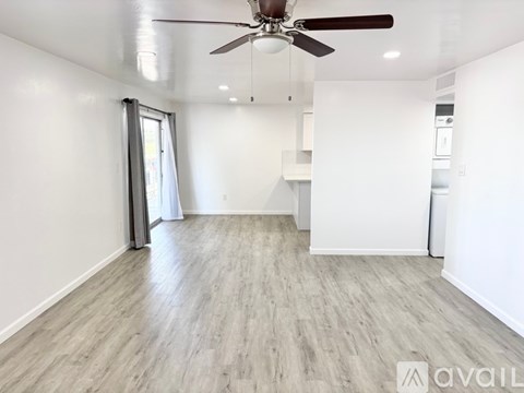 A spacious room with a ceiling fan and lighting, featuring a grey floor and white walls.