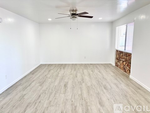 A spacious room with a ceiling fan and lighting, featuring a wood floor and a window with blinds.