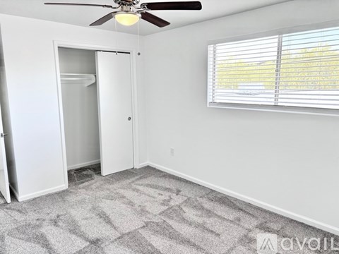 A room with a ceiling fan, a window with blinds, and a carpeted floor.