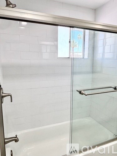 A glass shower door in a white tiled bathroom.