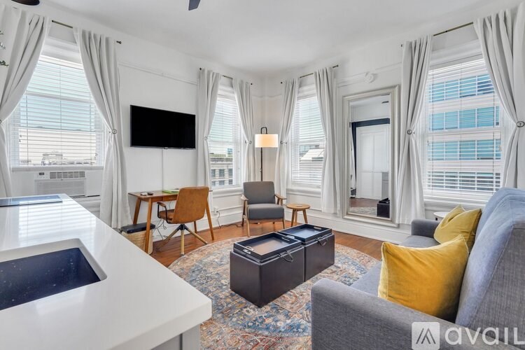 A living room with a grey sofa, a white table, and a flat-screen TV mounted on the wall.