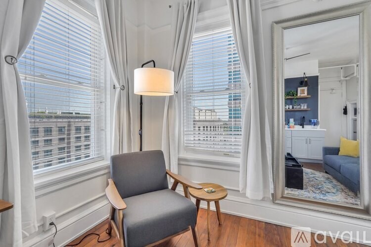 A grey chair is in front of a window with white curtains.