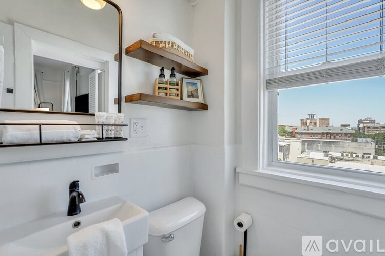 A bathroom with a white sink, toilet, and a window with a view of buildings outside.