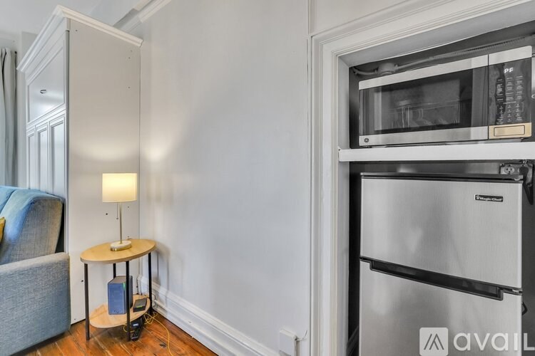 A kitchen area with a refrigerator, a table with a lamp, and a chair.