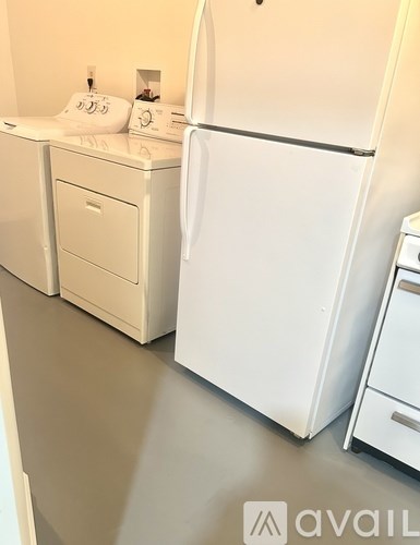 A white fridge stands next to a white washing machine and a white dishwasher in a kitchen.