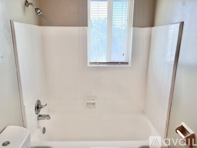 A white bathtub with a shower head and a toilet in a bathroom.