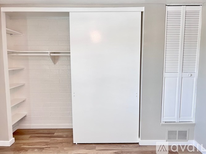 A white refrigerator is in a kitchen with white walls and wooden floors.