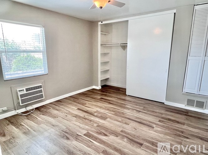 A room with a window, a wall-mounted air conditioner, and a wooden floor.