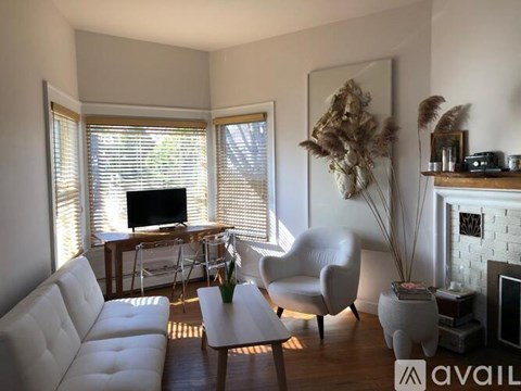 A living room with a white couch, a white chair, a coffee table, a fireplace, and a painting on the wall.