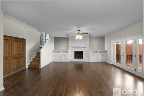 A spacious living room with wood flooring and a staircase leading to the upper level.
