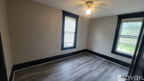 A room with a ceiling fan and two windows.