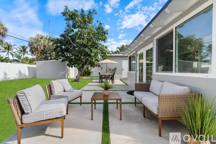 A patio with a white wall and a wooden table with chairs.