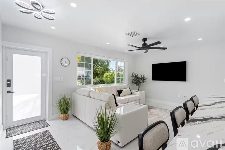 A modern living room with a white sofa, a ceiling fan, and a flat-screen TV mounted on the wall.