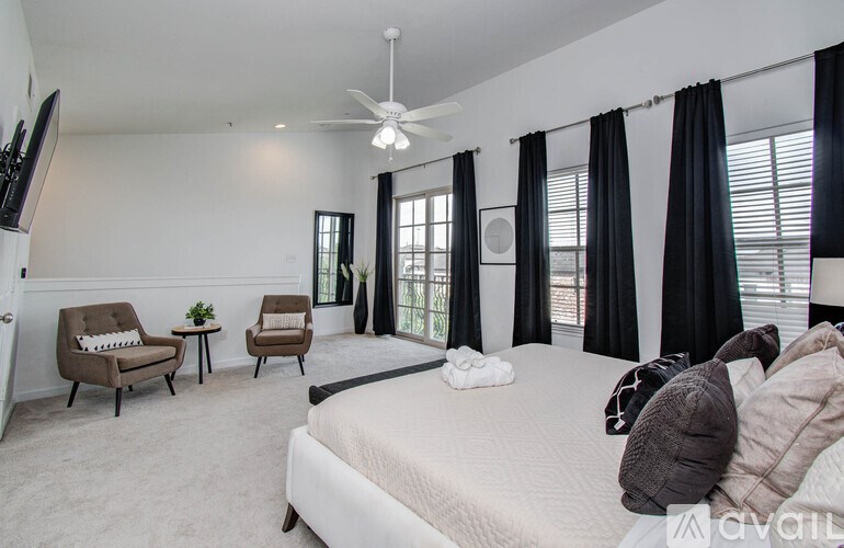 A bedroom with a bed, two chairs, and a ceiling fan.