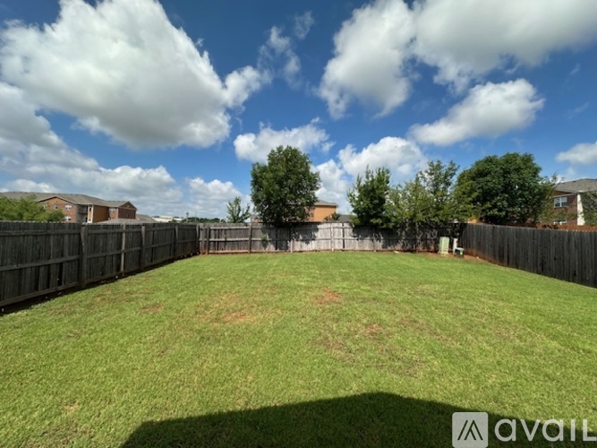 A backyard with a fence and trees under a blue sky with clouds.