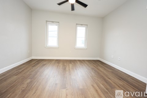 A room with wooden flooring and two windows.