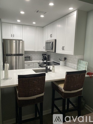 A kitchen with white cabinets and a countertop with two chairs.