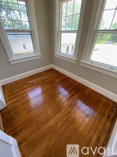 A room with wooden flooring and two windows.